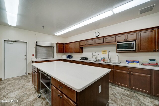 kitchen with stainless steel microwave, light tile patterned flooring, a center island, and sink