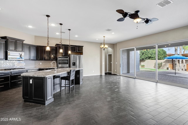 kitchen featuring appliances with stainless steel finishes, a kitchen breakfast bar, decorative backsplash, hanging light fixtures, and a kitchen island with sink