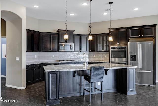 kitchen featuring pendant lighting, tasteful backsplash, an island with sink, light stone counters, and stainless steel appliances