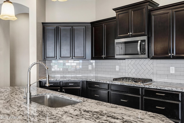 kitchen with sink, backsplash, dark brown cabinets, stainless steel appliances, and light stone counters