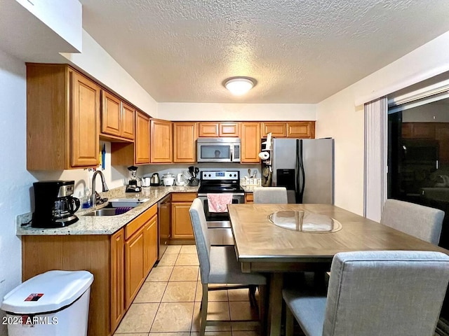 kitchen with appliances with stainless steel finishes, light tile patterned flooring, sink, and a textured ceiling