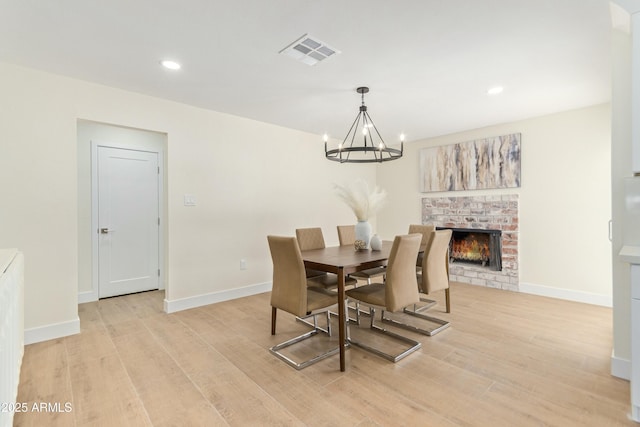 dining space with a fireplace, light wood-type flooring, and a notable chandelier