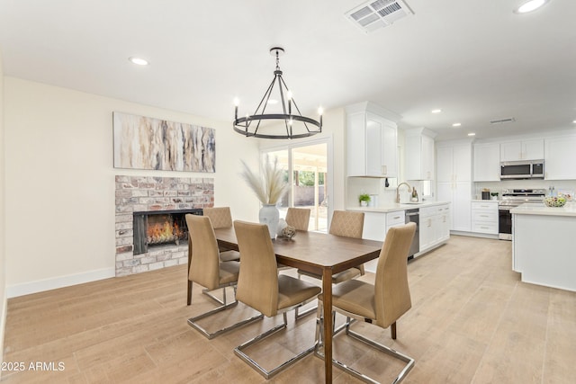 dining area featuring light hardwood / wood-style floors, a brick fireplace, and a notable chandelier