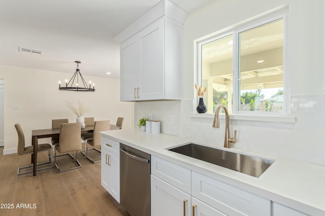 kitchen featuring dishwasher, white cabinets, sink, hanging light fixtures, and light hardwood / wood-style flooring