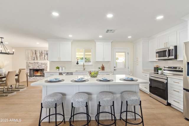 kitchen with white cabinetry, stainless steel appliances, light hardwood / wood-style flooring, an island with sink, and decorative light fixtures