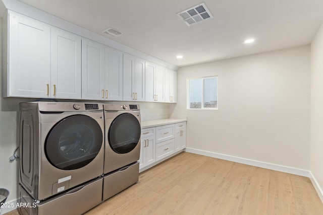 laundry area with cabinets, independent washer and dryer, and light hardwood / wood-style flooring