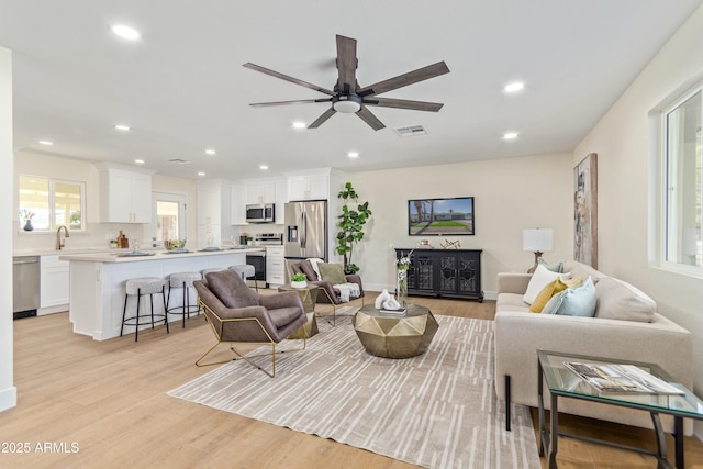 living room featuring ceiling fan, light wood-type flooring, and sink