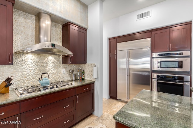 kitchen featuring stainless steel appliances, wall chimney exhaust hood, dark stone countertops, and tasteful backsplash