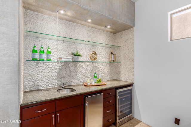 bar with light stone counters, stainless steel refrigerator, decorative backsplash, sink, and beverage cooler