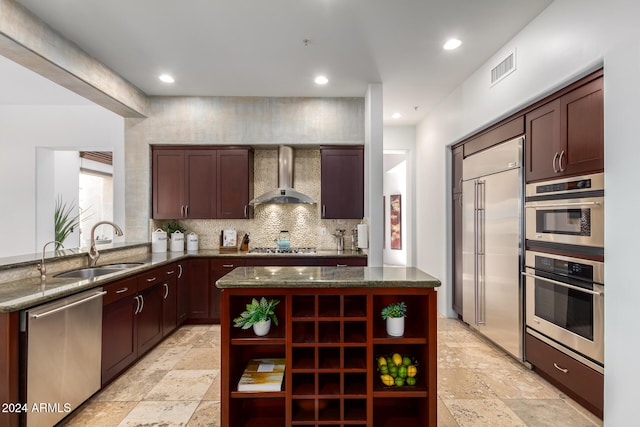 kitchen with stainless steel appliances, wall chimney exhaust hood, a kitchen island, and dark stone countertops