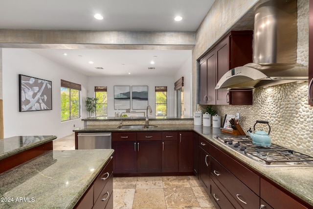 kitchen with stainless steel appliances, sink, kitchen peninsula, light stone counters, and wall chimney range hood