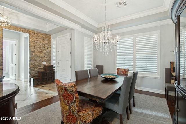 dining room with wood finished floors, visible vents, ornamental molding, a tray ceiling, and an inviting chandelier