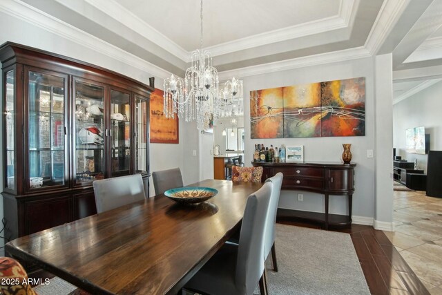 dining space with wood finished floors, baseboards, ornamental molding, a tray ceiling, and an inviting chandelier