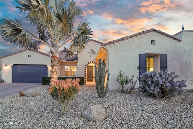 mediterranean / spanish home featuring a garage, a tile roof, driveway, and stucco siding