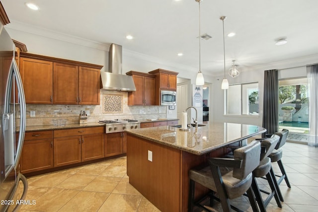 kitchen featuring visible vents, appliances with stainless steel finishes, brown cabinetry, a sink, and wall chimney exhaust hood