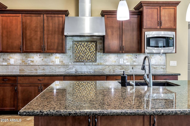 kitchen with wall chimney range hood, stainless steel microwave, dark stone countertops, and backsplash