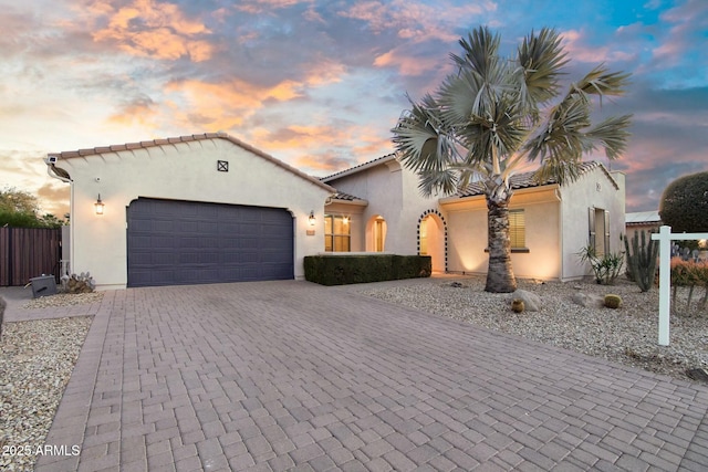 mediterranean / spanish-style home featuring a garage, fence, a tiled roof, decorative driveway, and stucco siding