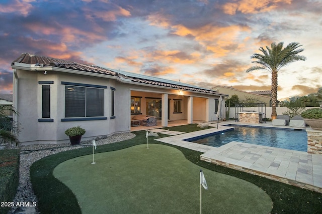 back of house at dusk featuring a fenced backyard, a tiled roof, a fenced in pool, stucco siding, and a patio area