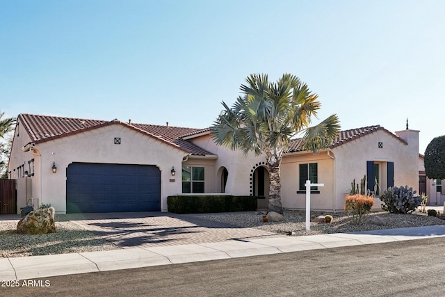 mediterranean / spanish house with an attached garage, driveway, a tiled roof, and stucco siding