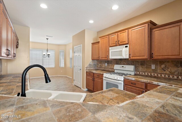 kitchen featuring white appliances, decorative backsplash, brown cabinetry, and a sink