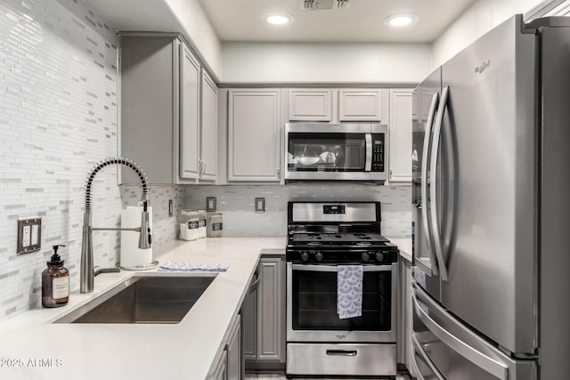 kitchen featuring visible vents, decorative backsplash, a sink, gray cabinetry, and stainless steel appliances