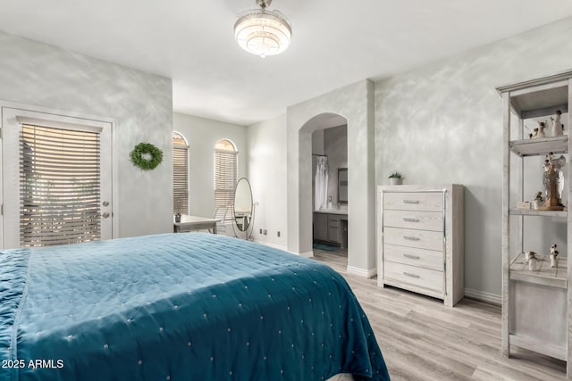 bedroom featuring access to outside, arched walkways, baseboards, wood finished floors, and ensuite bathroom