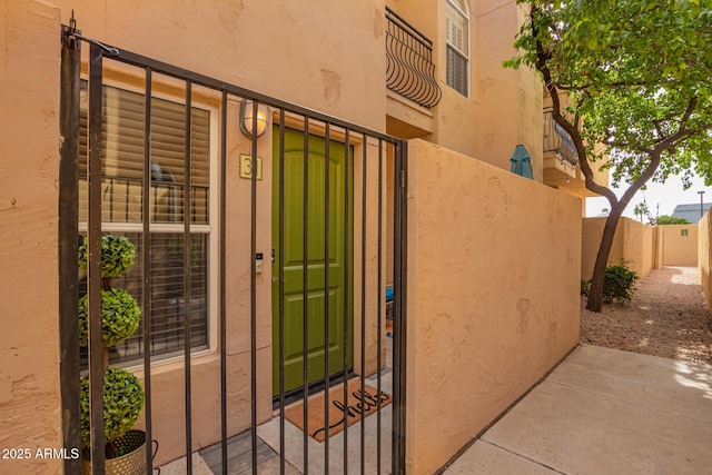 view of exterior entry featuring a gate, stucco siding, and fence