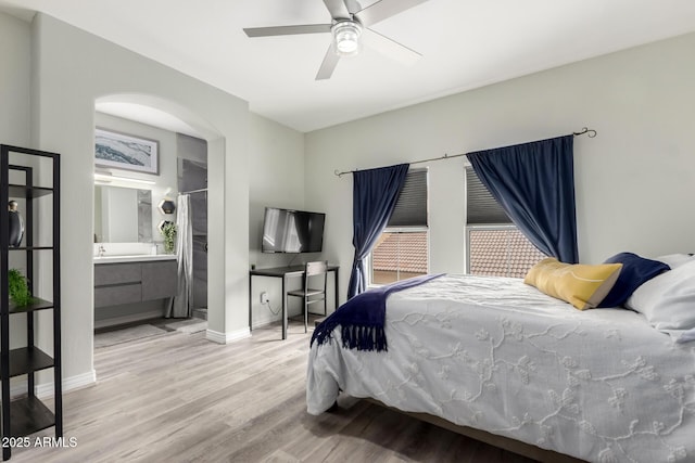 bedroom featuring ceiling fan, arched walkways, wood finished floors, baseboards, and ensuite bath