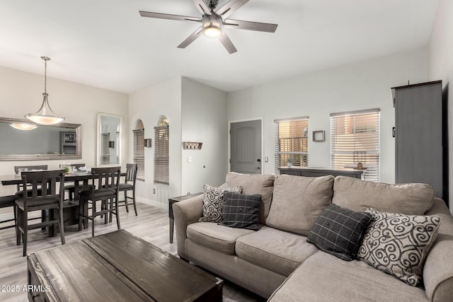 living area featuring baseboards, light wood finished floors, and ceiling fan