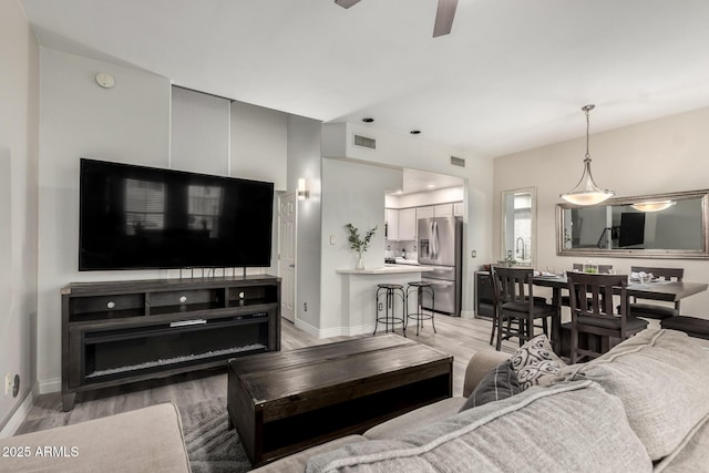 living area with visible vents, a ceiling fan, light wood finished floors, and baseboards