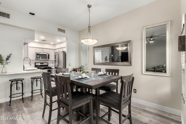 dining room featuring baseboards, a ceiling fan, light wood-style flooring, and visible vents