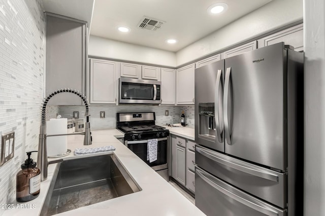 kitchen with decorative backsplash, visible vents, appliances with stainless steel finishes, a sink, and gray cabinetry