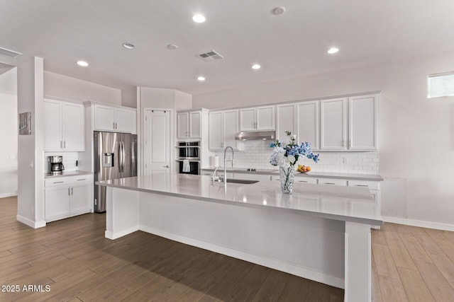 kitchen with appliances with stainless steel finishes, white cabinets, a sink, and a spacious island