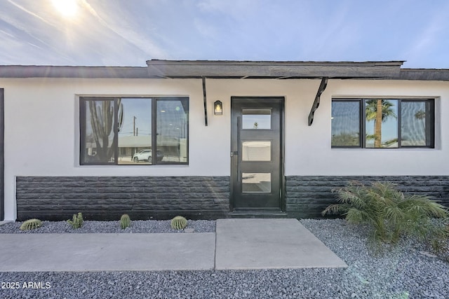 doorway to property featuring stone siding and stucco siding