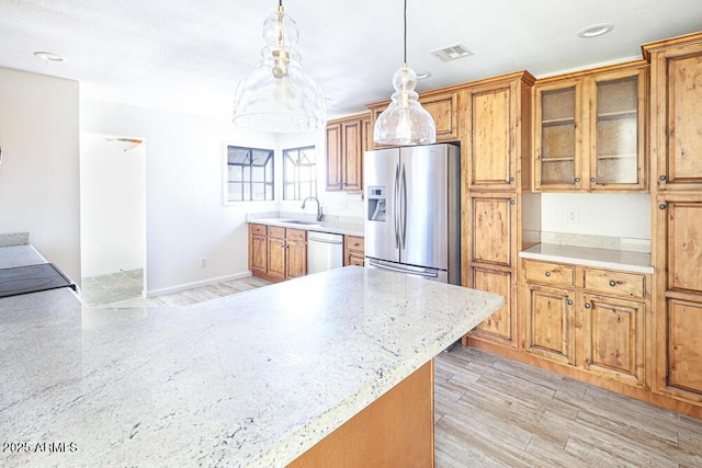 kitchen with brown cabinetry, visible vents, a sink, hanging light fixtures, and stainless steel appliances