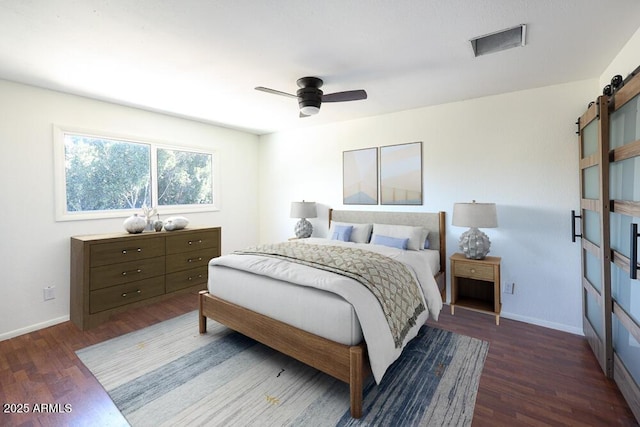 bedroom with a barn door, baseboards, visible vents, and wood finished floors