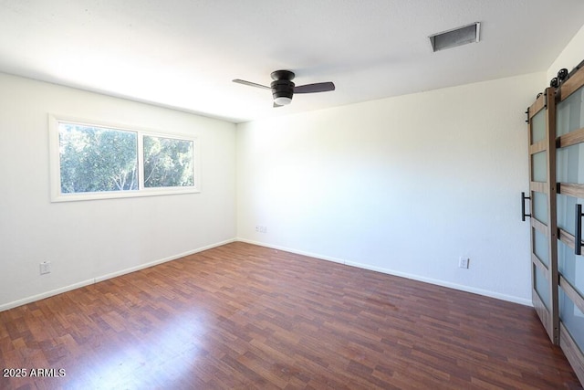 unfurnished room with visible vents, a ceiling fan, wood finished floors, a barn door, and baseboards