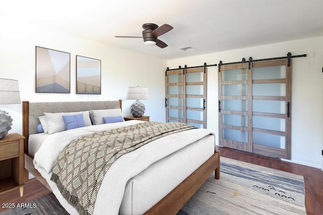 bedroom with a barn door, wood finished floors, visible vents, and ceiling fan