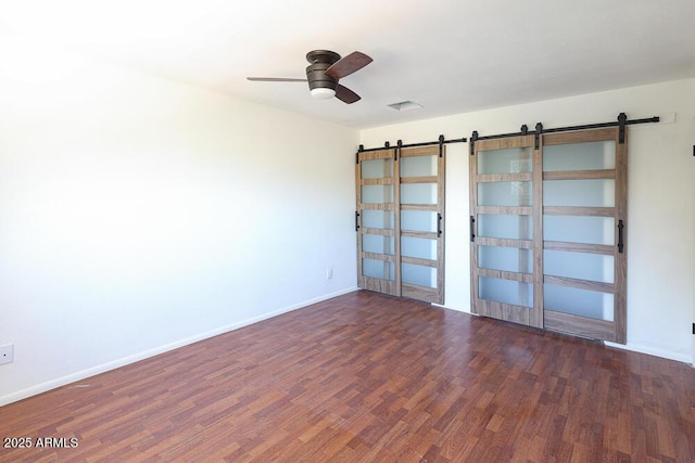 spare room featuring wood finished floors, a ceiling fan, baseboards, visible vents, and a barn door