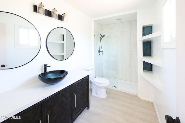 bathroom featuring a tile shower, toilet, vanity, and wood finished floors