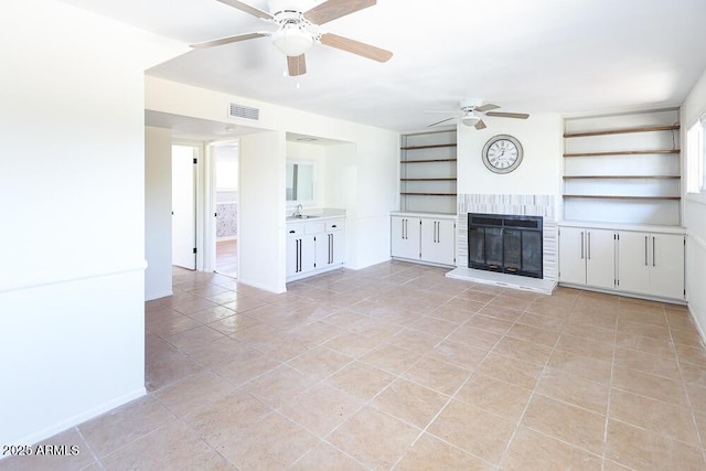 unfurnished living room featuring visible vents, built in shelves, light tile patterned flooring, a fireplace, and ceiling fan