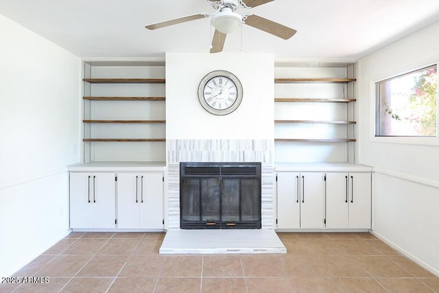 unfurnished living room with light tile patterned flooring, a glass covered fireplace, and ceiling fan