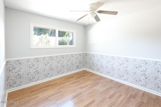 empty room featuring a ceiling fan, baseboards, wallpapered walls, light wood-style floors, and wainscoting