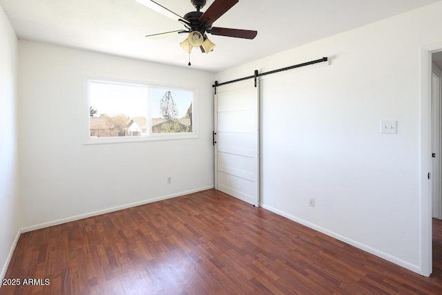 unfurnished bedroom featuring ceiling fan, baseboards, a barn door, and wood finished floors