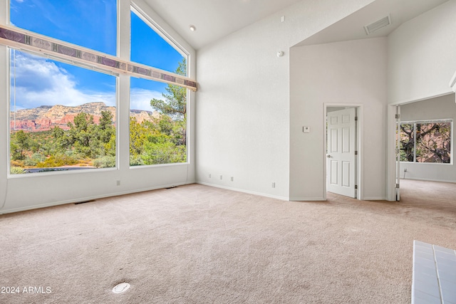 carpeted empty room with high vaulted ceiling, a wealth of natural light, and a mountain view