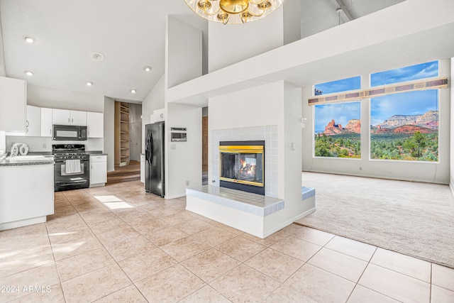 kitchen featuring high vaulted ceiling, black appliances, white cabinets, light carpet, and a tiled fireplace