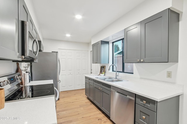 kitchen with stainless steel appliances, sink, gray cabinetry, and light wood-type flooring