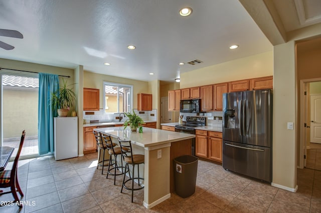 kitchen featuring decorative backsplash, a kitchen island, light countertops, black appliances, and a kitchen bar