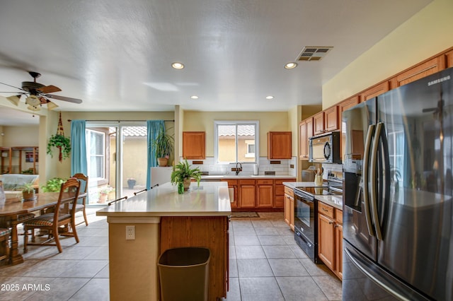 kitchen featuring tasteful backsplash, visible vents, a center island, light countertops, and black appliances