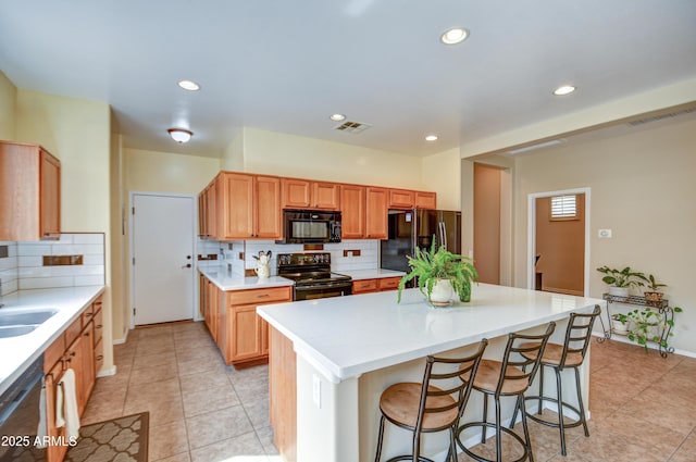 kitchen with visible vents, a center island, black appliances, a kitchen bar, and a sink